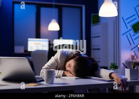 Entrepreneur working overtime on marketing project, falling asleep on desk while looking at financial documents trying to respect the deadline. Employee using modern technology network wireless Stock Photo