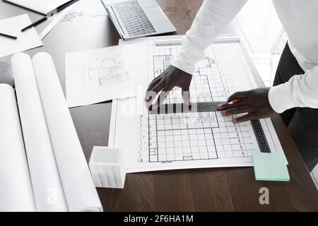 Close-up of African architect using pencil and ruler and drawing blueprint at his workplace at office Stock Photo