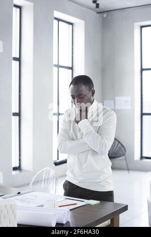 African pensive businessman standing near the office table and looking at blueprints with thoughtful sight Stock Photo