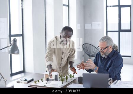 Two engineers sitting at the table and discussing construction of new building together at office Stock Photo