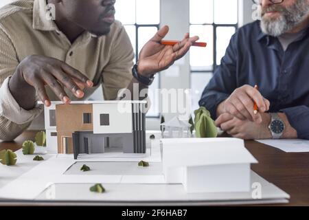 Close-up of carton model of new building on the table with two architects talking to each other in the background Stock Photo