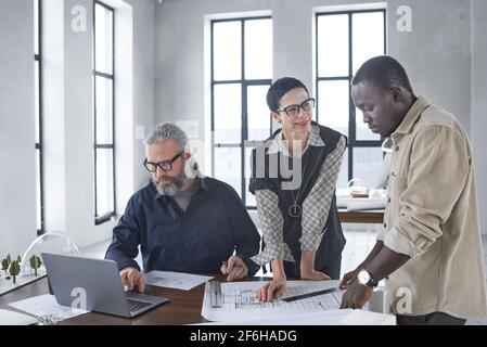 Group of architects working in team at the table they using laptop and drawing blueprints at office Stock Photo