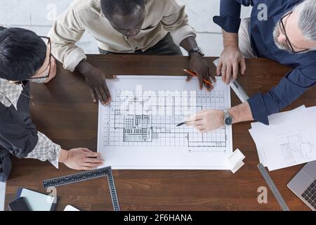 High angle view of blueprint on the table with engineers examining it and discussing in team at office Stock Photo