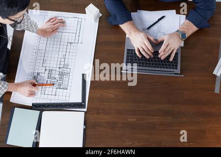 High angle view of engineers working on laptop and drawing blueprint of new construction at the wooden table Stock Photo