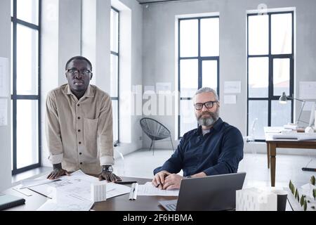 Portrait of two confident businessmen looking at camera while working with blueprints together at office Stock Photo