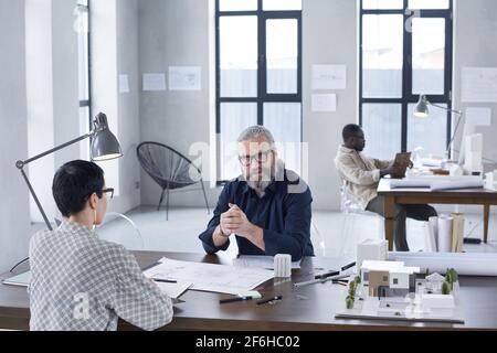 Group of engineers sitting at the table at meeting and working with blueprints at modern office Stock Photo
