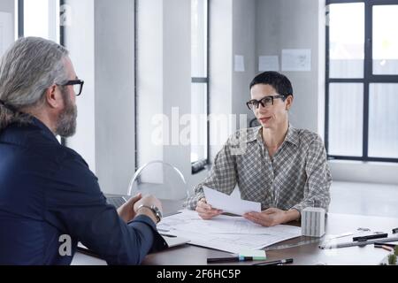 Two business partners sitting at the table and discussing business project together during meeting at office Stock Photo