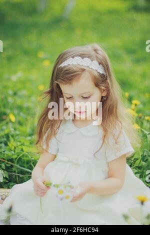 A girl in dress holds a bouquet of daisies in spring cherry garden Stock Photo