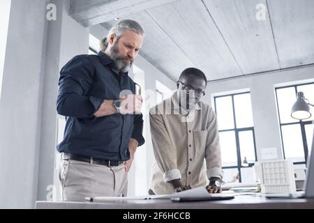Two architects working in team standing near the table with blueprints and examining them at office Stock Photo