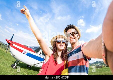 Young couple taking selfie with lightweight airplane - Happy people boarding on excursion air plane - Alternative adventure vacation concept Stock Photo