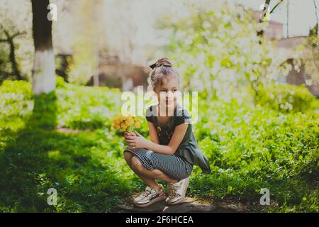 A girl in dress holds a bouquet of yellow dandelions in spring cherry garden Stock Photo