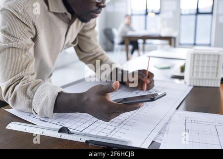 Close-up of African engineer drawing a blueprint at the table using his mobile phone at work Stock Photo
