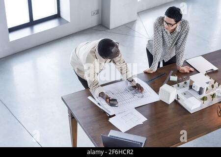High angle view of two engineers developing new project together they working over blueprints and model of building Stock Photo