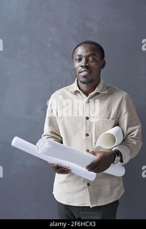 Portrait of African American architect holding blueprint and looking at camera standing against the grey background Stock Photo