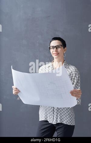 Portrait of mature female architect holding blueprint and looking at camera isolated on black background Stock Photo