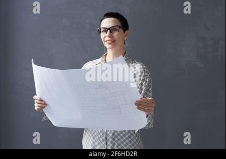 Portrait of mature architect in eyeglasses examining blueprint and looking at camera against the black background Stock Photo