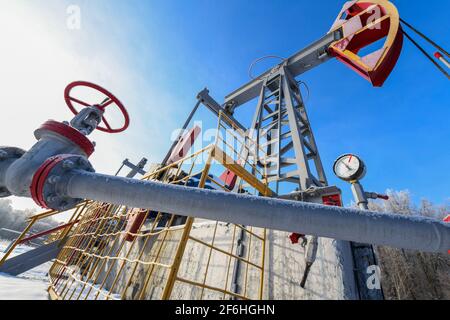 Oil pumpjack winter work. Oil pressure gauge shows 10 ATM (Max 15 Bar - red line). A pumpjack is the overground drive for a reciprocating piston pump Stock Photo