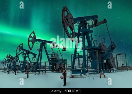 Oil pump - Nodding donkey. Night view. Oil industry equipment. Oil field pump jack and oil refinery in the winter with snow, mountains and forest in b Stock Photo