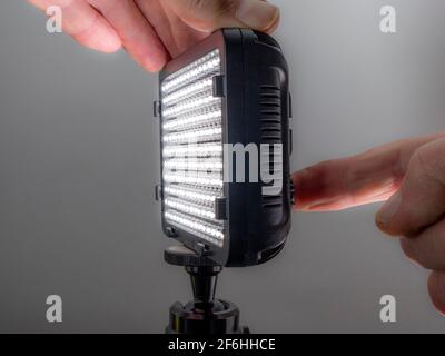 Closeup of a man’s hands pressing the button on the back of a small, battery operated, portable LED light, for photo / video, while it switches on. Stock Photo