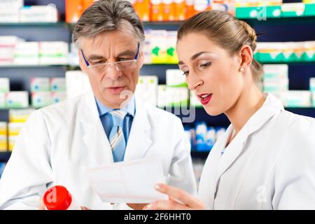 Two pharmacists with pharmaceuticals in hand consulting each other in a pharmacy Stock Photo