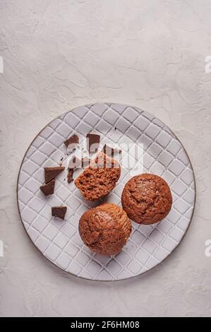 Homemade chocolate cupcakes and pieces of chocolate in textured plate on wooden light background, vertical orientation, copy space Stock Photo