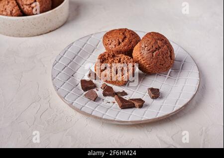 Homemade chocolate cupcakes and pieces of chocolate in textured plate on wooden light background, top view, copy space Stock Photo
