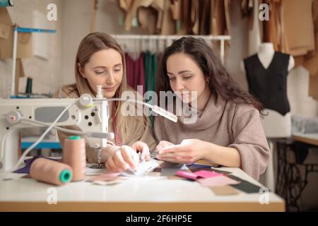 two femail Dressmakers or tailors or fashiondesigners or seamstresses working with sewing machine atv workshop studio. Stock Photo