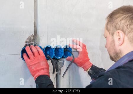The electrician inserts the plastic box directly into the outlet holes. Close-up Stock Photo