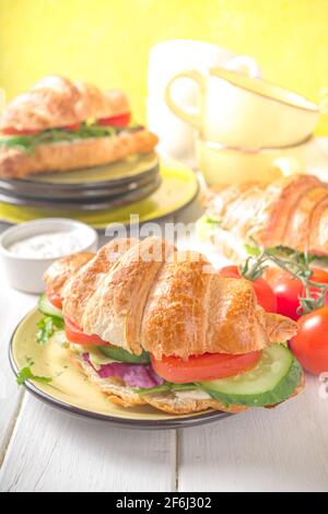 Croissant sandwich with fresh vegetables - lettuce, tomatoes, cucumbers. Vitamin diet summer or spring snack, breakfast. On yellow background copy spa Stock Photo