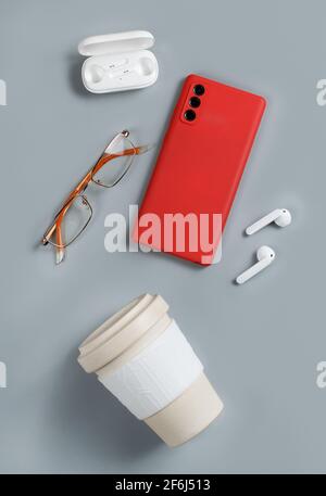 Smartphone, reusable coffee cup, wireless earphones and glasses on grey background top view Stock Photo