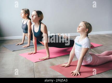 Three teenage girls sisters in sportswear doing yoga and stretching on mats in the gym. Healthy sports lifestyle, body care, morning gymnastics routin Stock Photo