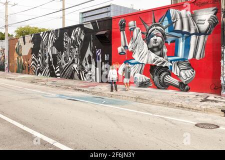 A couple walks down a street with street art covering every wall in sight in the Wynwood Art District, Miami, Florida, USA Stock Photo