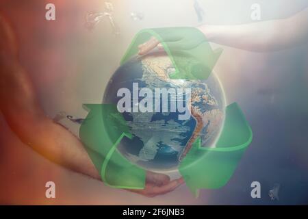 Women's and men's hands support the globe of planet Earth with sign of recycle. Around the flying plastic debris. The concept of preserving the earth' Stock Photo