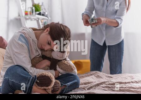 upset teenage girl hugging teddy bear near mother on blurred background Stock Photo