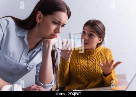 worried mother near displeased teenage daughter gesturing on blurred background Stock Photo