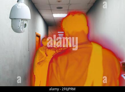 A queue of people in a narrow space under the supervision of a video camera in a color filter. Rear view. CCTV concept. Stock Photo