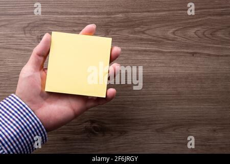 Hand holding sticky post note paper sheet on wooden background Stock Photo