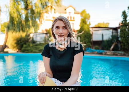 An elegant woman looks away in surprise. In the background there is a pool and a house. Concept of human emotions and expressions. Stock Photo