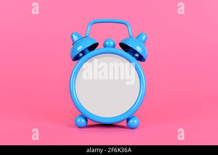 Blue classic alarm clock without hands and numbers on pink background. Stock Photo
