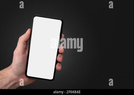 Man hand holding the black cell phone smartphone with blank white screen and modern frame less design on black background. Mockup phone. hand holding Stock Photo