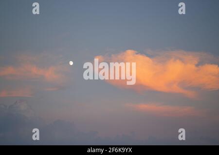 Blue sky and orange clouds. Sunset sky with the moon, the clouds are colored in orange. Stock Photo