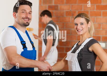Three people - one woman and two men - renovating an apartment; the couple in front are shaking hands Stock Photo