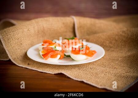 halves of boiled eggs with pieces of salted salmon on a wooden table Stock Photo