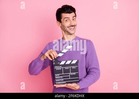 Photo of funny sweet young man dressed purple pullover holding clapperboard isolated pink color background Stock Photo