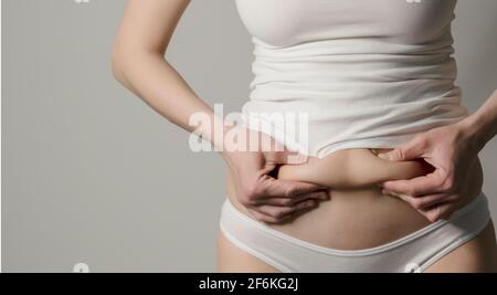 Skinny fat figured unrecognizable woman clipping her belly fat. Woman`s  figure closeup raw studio shot in grey background. Dieting and fat loss  concep Stock Photo - Alamy