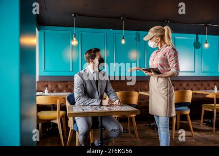 Conversation between a guest and a waiter in a restaurant at the time of the coronavirus. The female waiter talks to the businessman and recommends hi Stock Photo