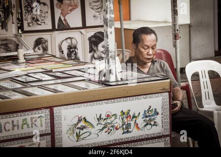 Chinatown, Singapore - December 25, 2013: One elderly man seated in a chair beside a street stall reading. Stock Photo