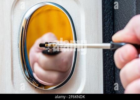 Close-up - a human hand inserts a key into the keyhole. Door furniture. Selective focus. Focus on the keyhole. Reflection. Stock Photo