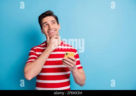 Photo portrait of young man using mobile phone looking empty space smiling touching face isolated on bright blue color background Stock Photo
