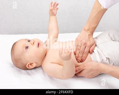 Female pediatrician or health care practitioner examines baby girl's abdomen. Doctor performing manual palpation. Child physical examination concept Stock Photo